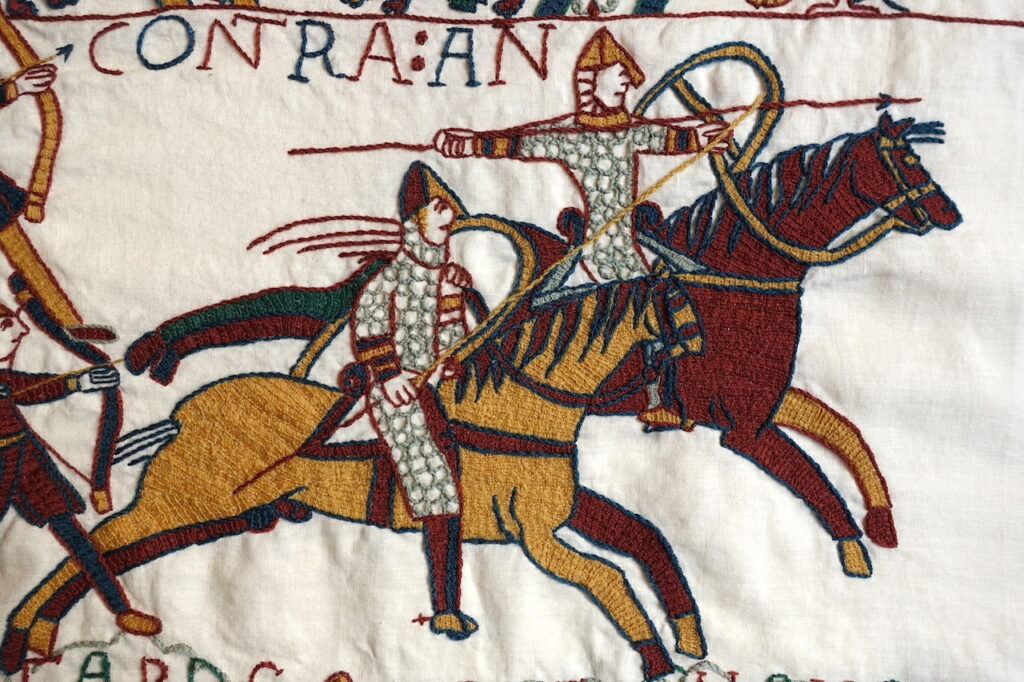 Two embroidered Norman horsemen, wielding spears and shields and wearing armour.