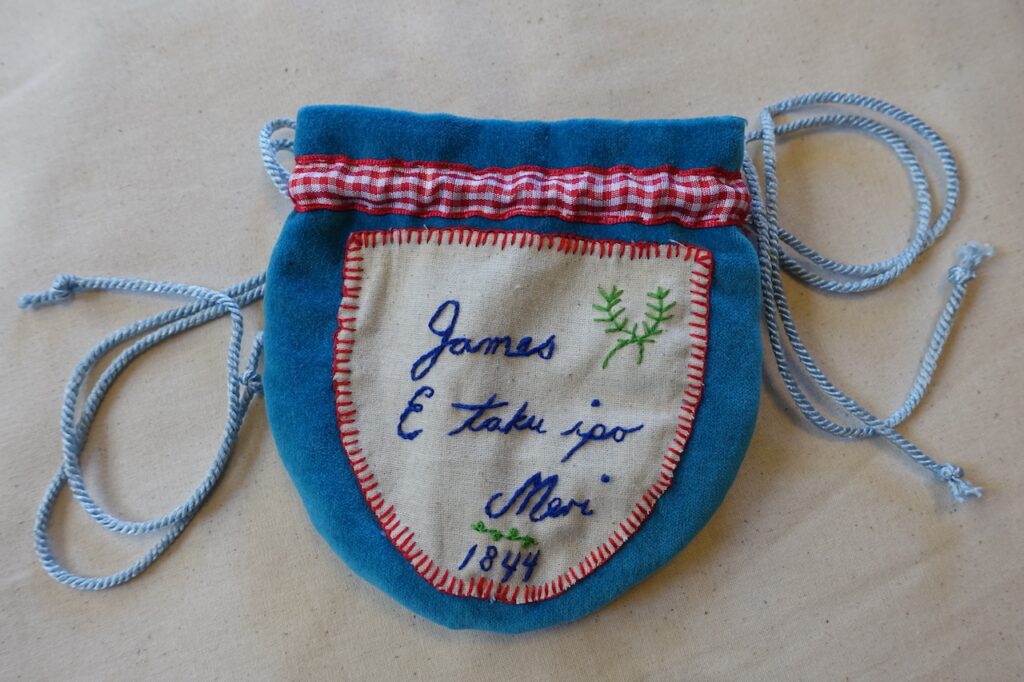 A small hand-made tobacco pouch make from blue velvet and embroidered with the words 'James E taku ipo Meri' and the date 1844.