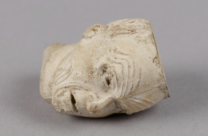 A white clay pipe bowl shaped into a tattooed Maori warrior's head with mouth open